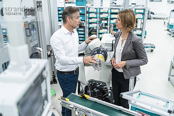 Geschäftsfrau und Mann unterhalten sich an einem Montageroboter in einer Fabrik