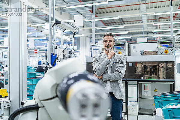 Porträt eines selbstbewussten Geschäftsmannes am Montageroboter in einer Fabrik