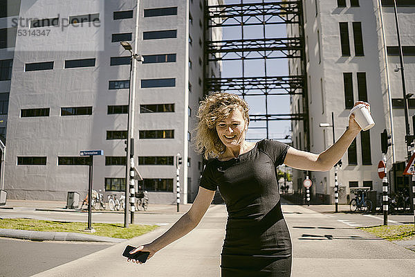 Porträt einer lächelnden reifen Geschäftsfrau mit Smartphone und Kaffee zum Balancieren im Freien