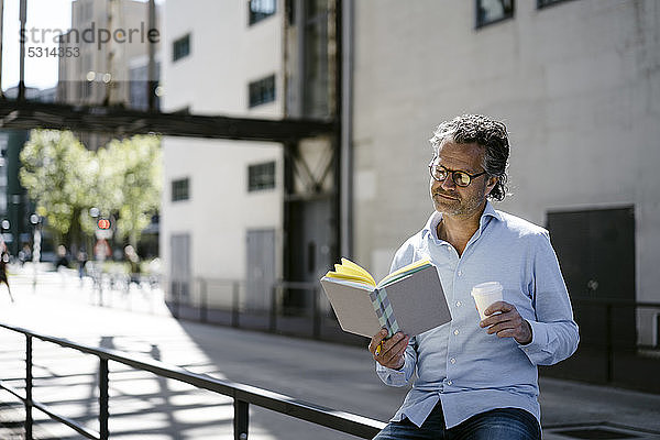 Porträt eines reifen Mannes  der ein Buch liest und eine Tasse Kaffee zum Mitnehmen hält