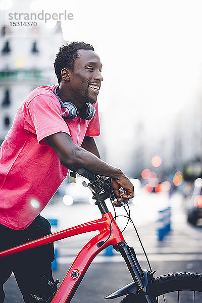 Glücklicher junger Mann mit E-Fahrrad in der Stadt