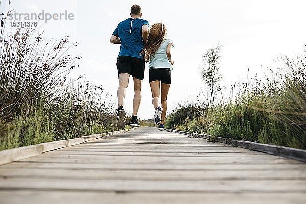 Rückansicht eines jungen Paares beim Joggen auf einem Holzlaufsteg