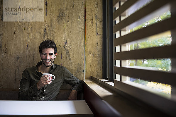 Porträt eines lachenden Mannes  der in einem Café Kaffee trinkt