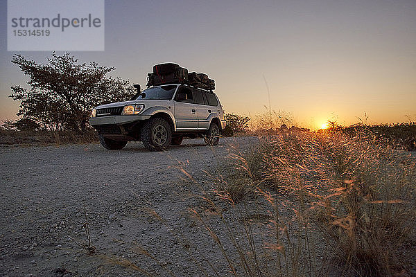 Geländewagen fährt bei Sonnenaufgang auf einer unbefestigten Straße  Makgadikgadi Pans  Botswana