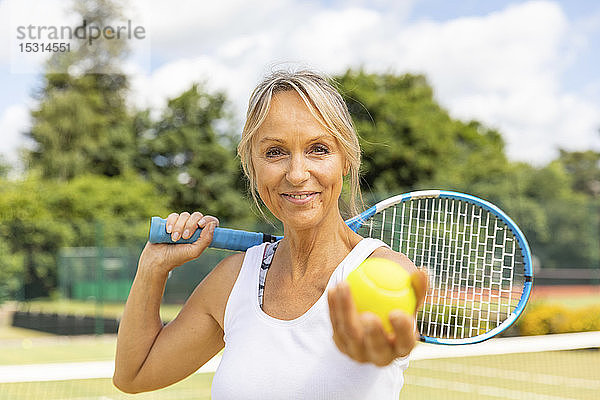 Porträt einer lächelnden reifen Frau  die im Tennisclub einen Tennisball hält