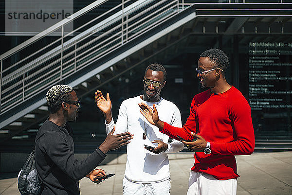 Drei coole junge Männer mit Mobiltelefonen treffen sich in der Stadt