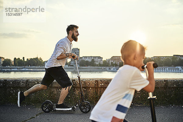 Vater und Sohn fahren Roller am Flussufer