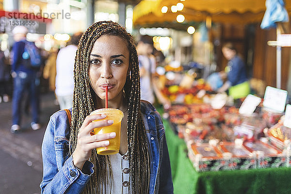 Porträt einer jungen Frau  die auf einem Straßenmarkt frischen Orangensaft trinkt  London  UK