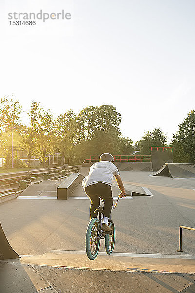 Rückansicht eines jungen Mannes auf einem BMX-Rad im Skatepark bei Sonnenuntergang