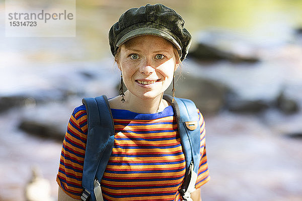 Porträt einer lächelnden Frau mit Rucksack an einem Flussufer