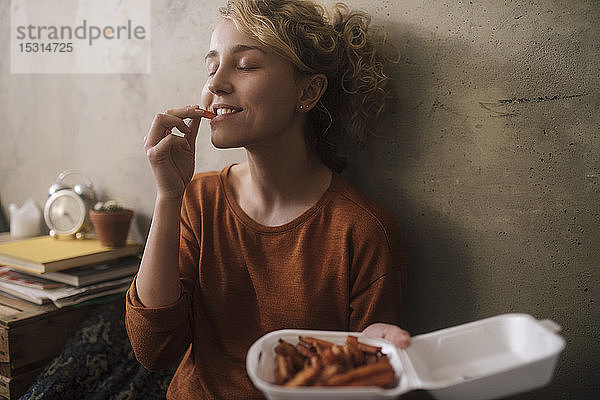 Porträt einer jungen Frau  die zu Hause Pommes Frites isst