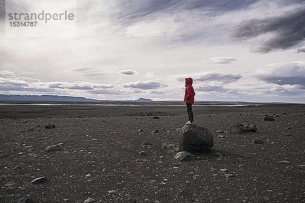 Junge Frau steht auf einem Felsen im vulkanischen Hochland von Island
