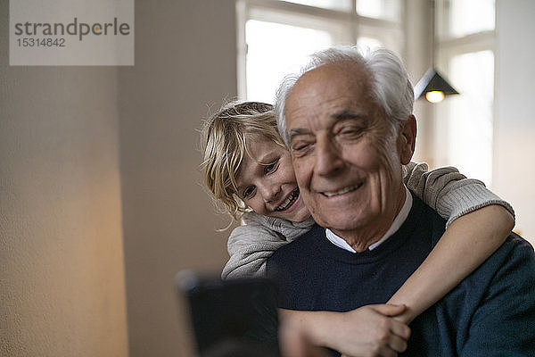 Glücklicher Enkel umarmt Großvater mit Handy zu Hause