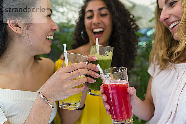 Drei glückliche junge Frauen stoßen mit gesunden Getränken an