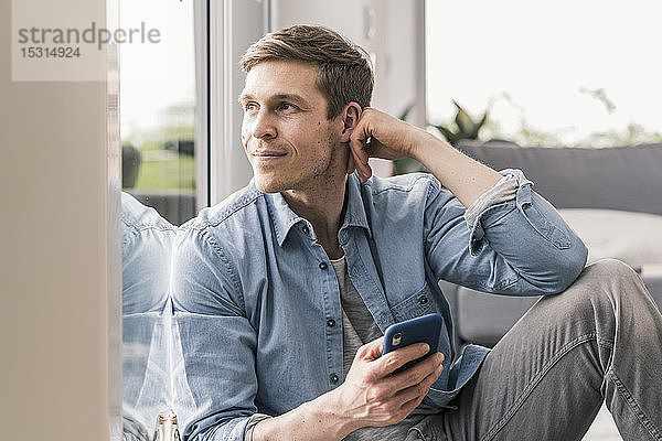 Mittelgroßer erwachsener Mann am Fenster sitzend  mit Smartphone