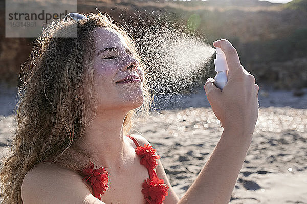 Junge Frau  die am Strand Sonnencremespray aufträgt