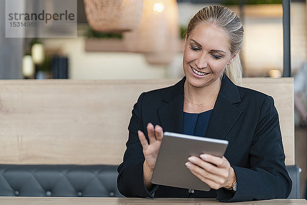 Porträt einer lächelnden blonden Geschäftsfrau mit digitalem Tablet in einem Café