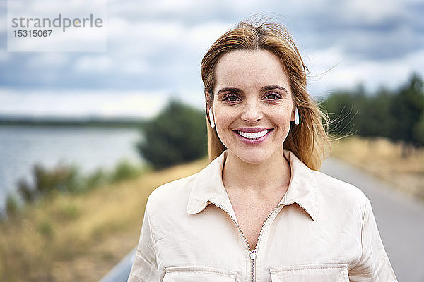 Porträt einer lächelnden Frau mit drahtlosen Kopfhörern in der Natur