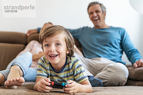 Junge liegt zu Hause auf der Couch und spielt Videospiel  während die Eltern zusehen