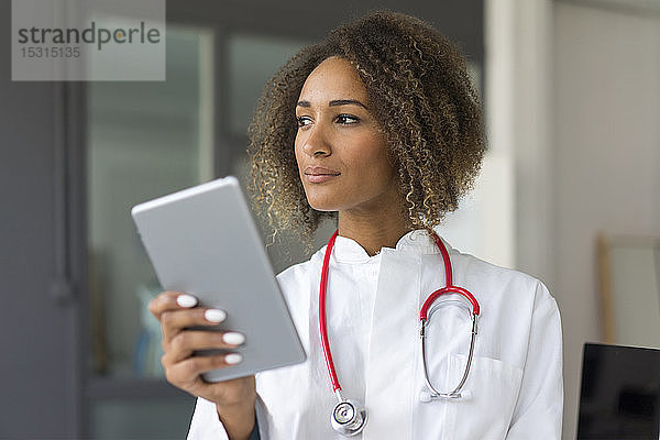 Porträt eines jungen Arztes mit Stethoskop und digitalem Tablett  der in die Ferne schaut