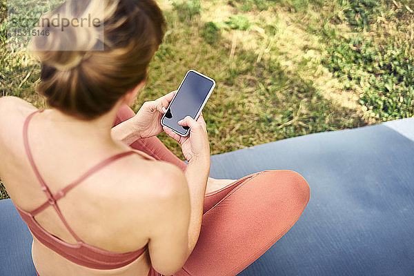 Frau benutzt Smartphone  während sie eine Pause vom Yoga im Freien macht