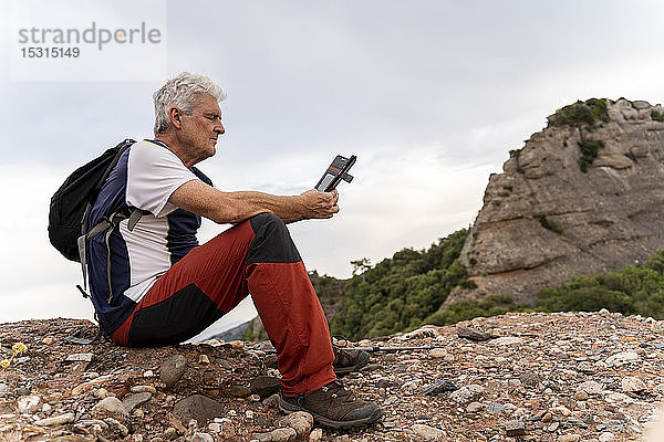 Senioren-Wanderer mit Smartphone  auf dem Aussichtspunkt sitzend