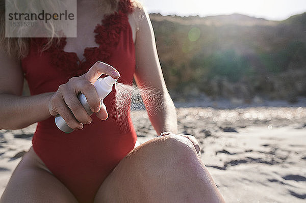 Junge Frau  die am Strand Sonnencremespray aufträgt