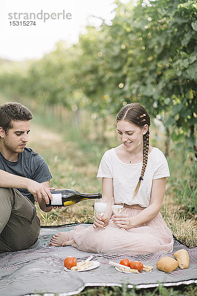 Glückliches junges Paar beim Picknick mit Prosecco in den Weinbergen