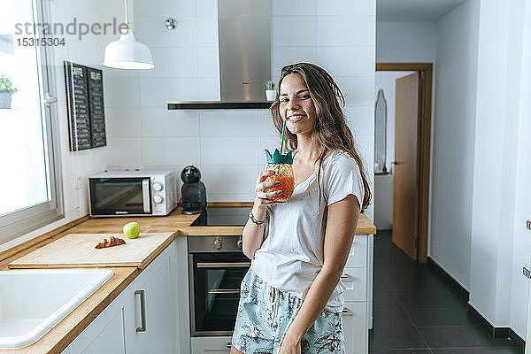 Porträt einer lächelnden jungen Frau bei einem Drink in der Küche