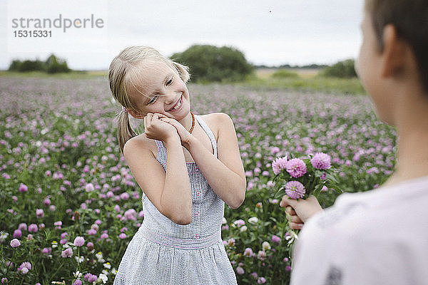 Junge schenkt lächelndem Mädchen Kleeblumen