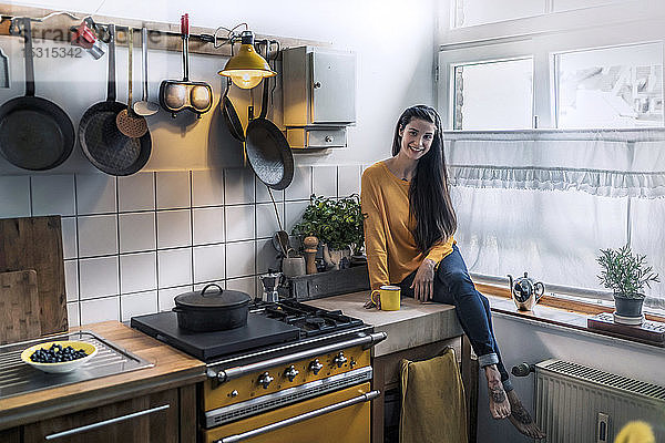 Porträt einer lächelnden jungen Frau  die zu Hause auf dem Küchentisch sitzt