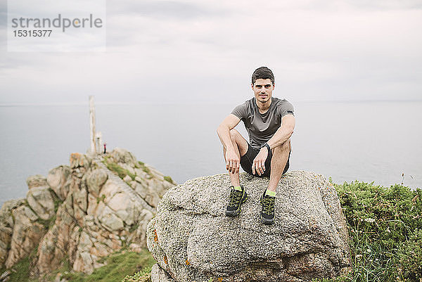 Porträt eines Trailrunners  der auf einem Felsen in der Küstenlandschaft sitzt  Ferrol  Spanien