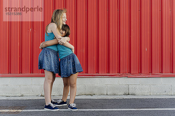 Schwestern umarmen sich vor einer roten Wand