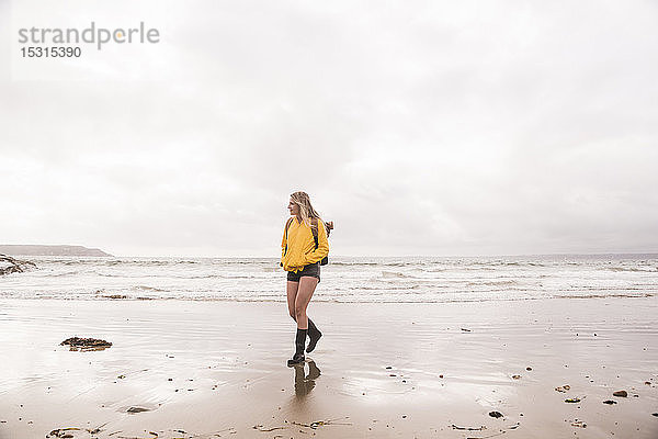 Frau mit gelber Regenjacke geht am Strand spazieren