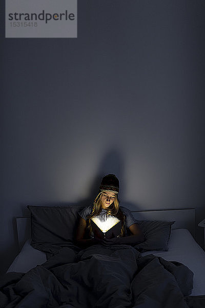 Junge Frau liest zu Hause im Bett ein illuminiertes Buch