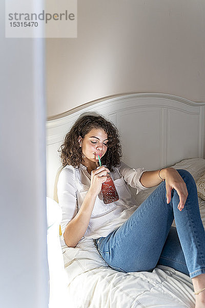 Entspannte junge Frau liegt mit gesundem Getränk im Bett