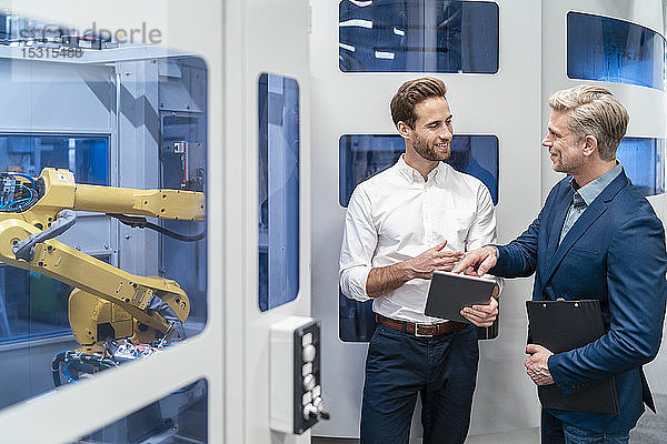 Zwei Geschäftsleute unterhalten sich an einem Roboter in einer modernen Fabrik