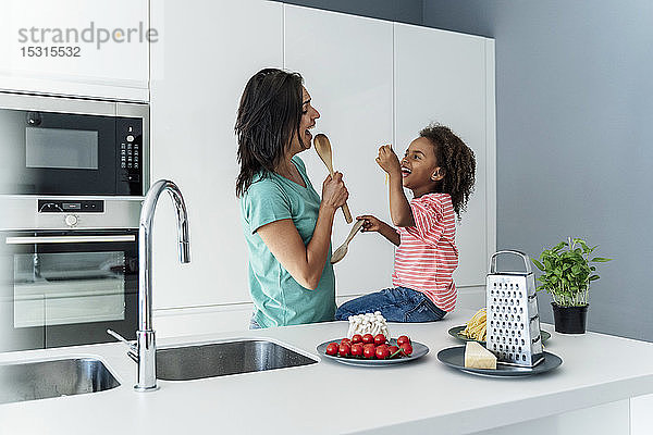 Mutter und Tochter kochen gemeinsam in der Küche und spielen mit Holzlöffeln