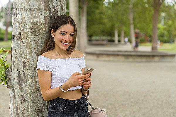 Porträt einer jungen Frau mit Smartphone im Park