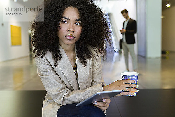 Junge Geschäftsfrau mit Kaffee und Tablette zum Mitnehmen in einem Foyer