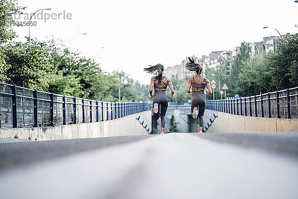 Oberflächenniveau von zwei sportlichen Zwillingsschwestern  die auf einer Straße laufen