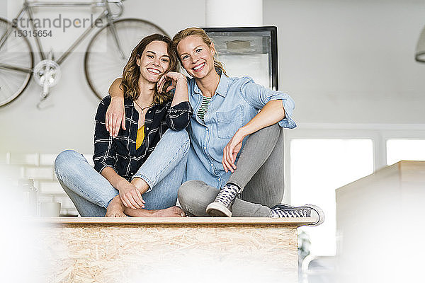 Zwei junge Frauen sitzen im Schneidersitz auf der Theke ihres Coffeeshops  mit ausgebreiteten Armen