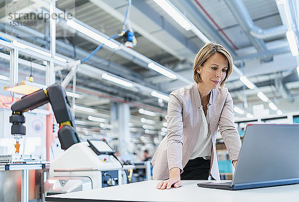Geschäftsfrau in einer modernen Fabrikhalle mit Laptop