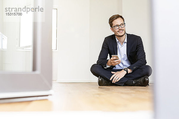 Lächelnder Geschäftsmann mit Handy auf dem Boden sitzend