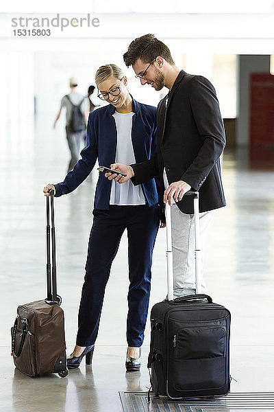 Zwei lächelnde junge Geschäftspartner mit einem Smartphone am Flughafen