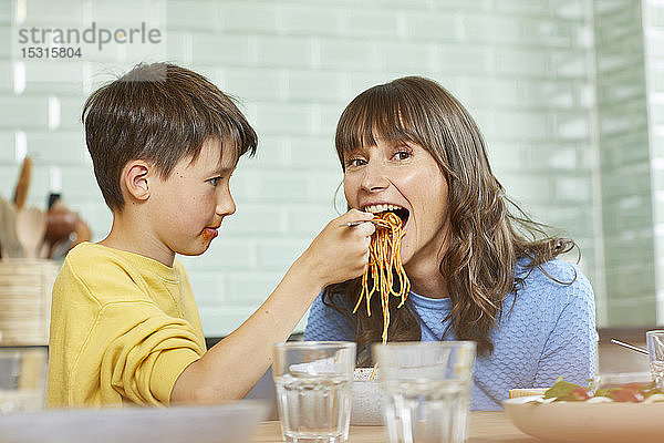 Sohn füttert Mutter mit Spaghetti in der Küche