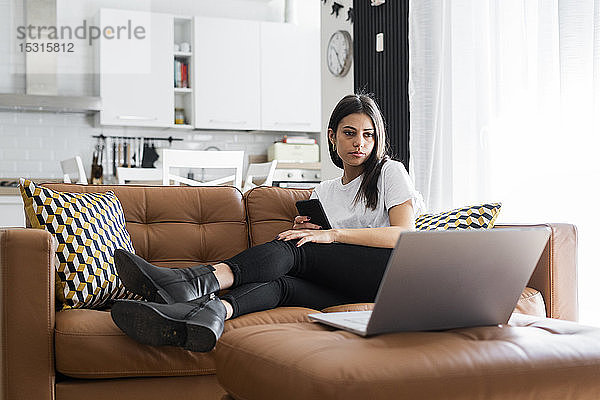 Junge Frau sitzt zu Hause auf einer Couch und benutzt einen Laptop