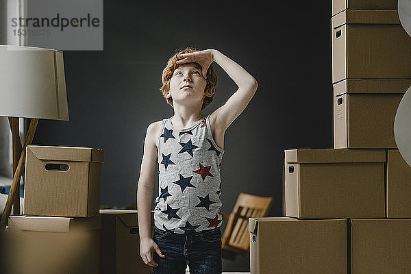 Porträt eines rothaarigen Jungen  der neben Pappkartons steht und nach oben schaut