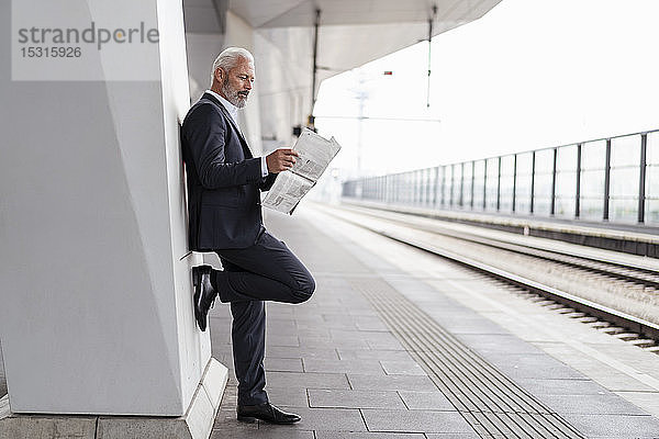 Älterer Geschäftsmann liest Zeitung auf dem Bahnsteig