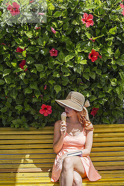 Frau mit Buch sitzt auf einer Bank und isst Eiscreme  Frigiliana  Malaga  Spanien